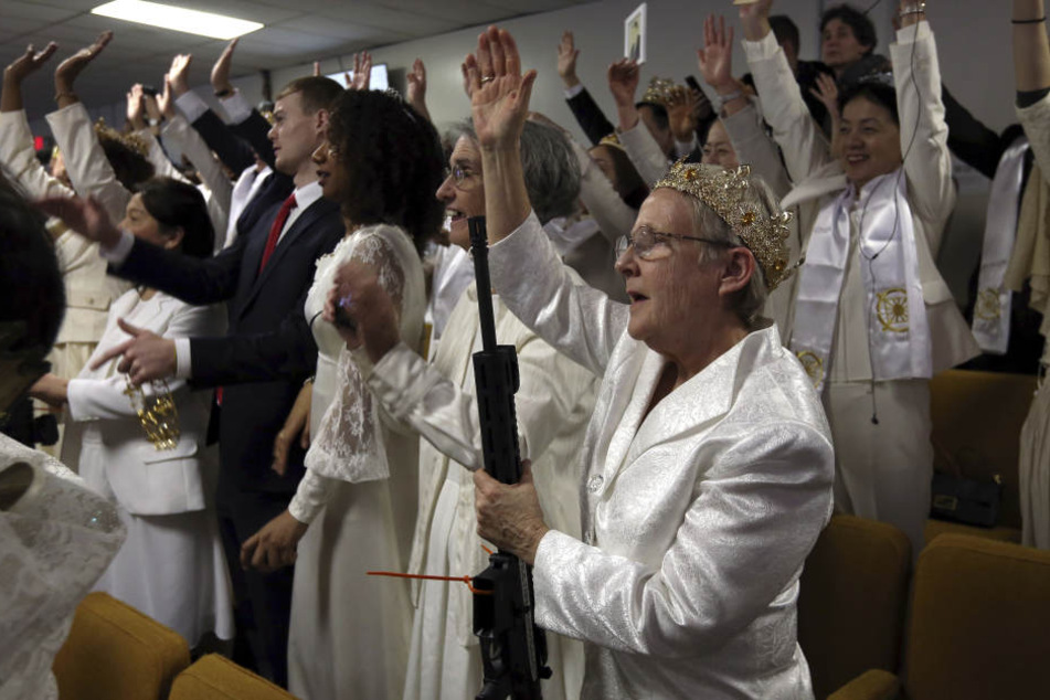 Eine Frau trägt eine Krone und hält jubelnd ein AR-15 Gewehr bei einem Gottesdienst in der Kirche World Peace and Unification Sanctuary.