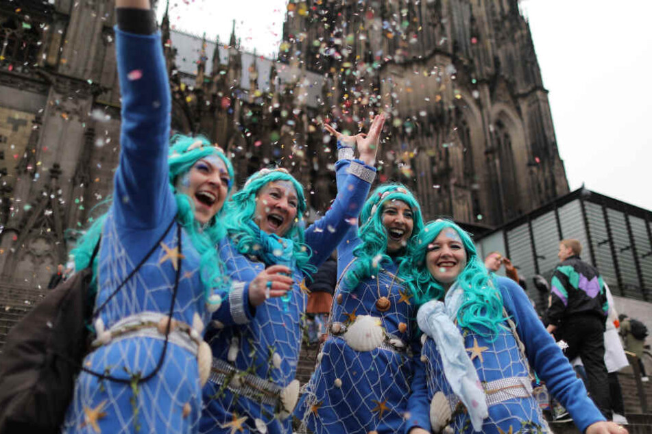 Karnevalistinnen feiern vor dem Kölner Dom und werfen Konfetti in die Höhe.