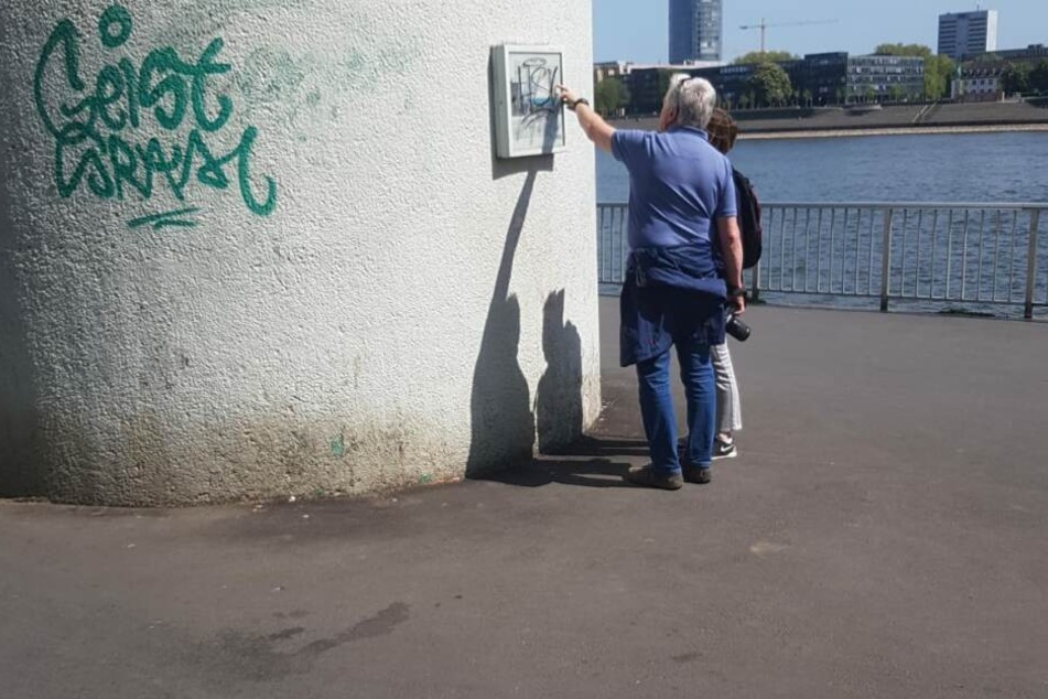 Touristen versuchen die Tafel am Pegel Köln zu lesen.
