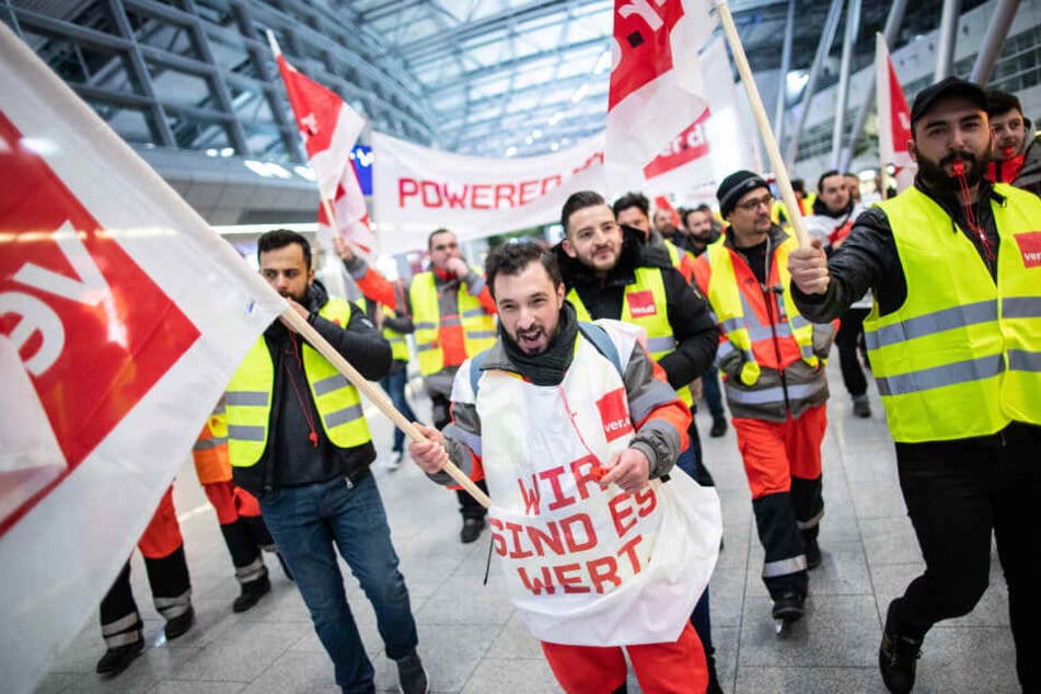 Gewerkschaftler von Verdi demonstrieren mit einem Plakat und Fahnen im Gebäude des Düsseldorfer Flughafens.