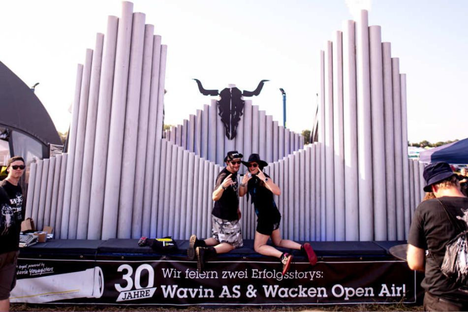 Zwei Wacken-Besucher lassen sich vor einer Holz-Skulptur fotografieren.