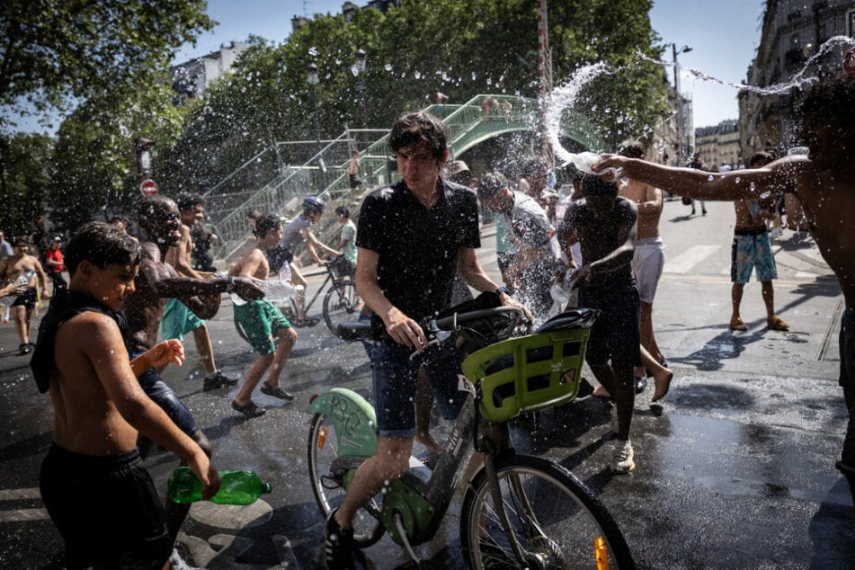 Eine Gruppe von Jugendlichen bespritzt einen Radfahrer mit Wasser.