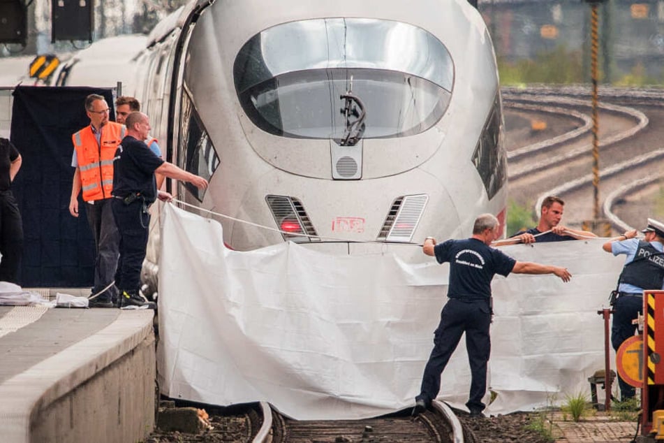 Polizisten und Feuerwehrleute spannen im Hauptbahnhof eine weiße Plane als Sichtschutz vor einen ICE.