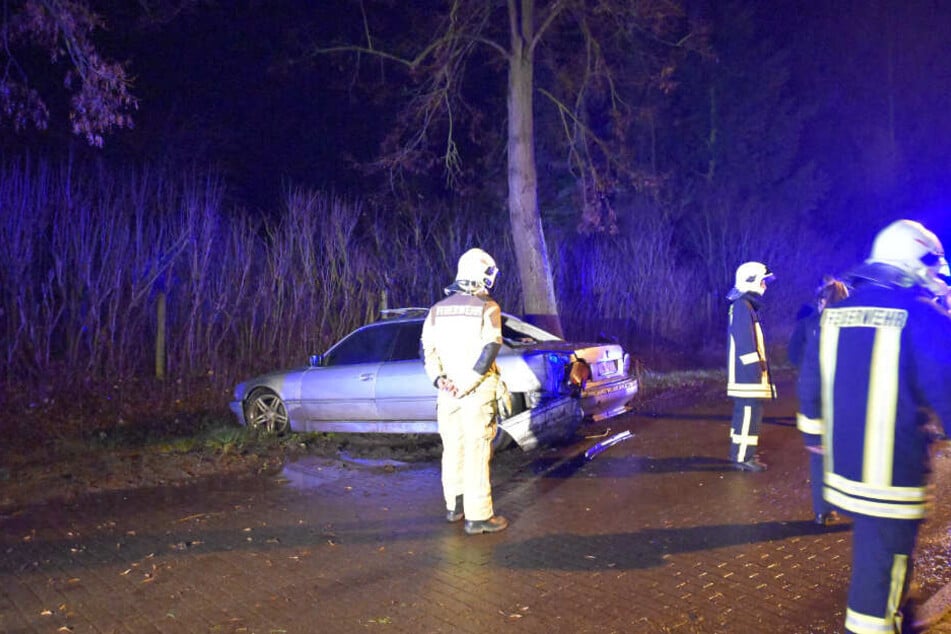 Einsatzkräfte der Feuerwehr stehen vor dem beschädigten Auto