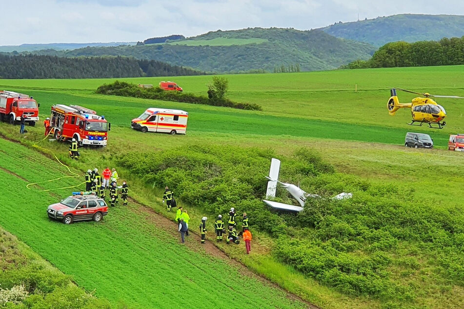Ein Rettungshubschrauber und Rettungsfahrzeuge stehen an der Absturzstelle. Bei dem Unglück nahe Bad Sobernheim sind zwei Menschen schwer verletzt worden.