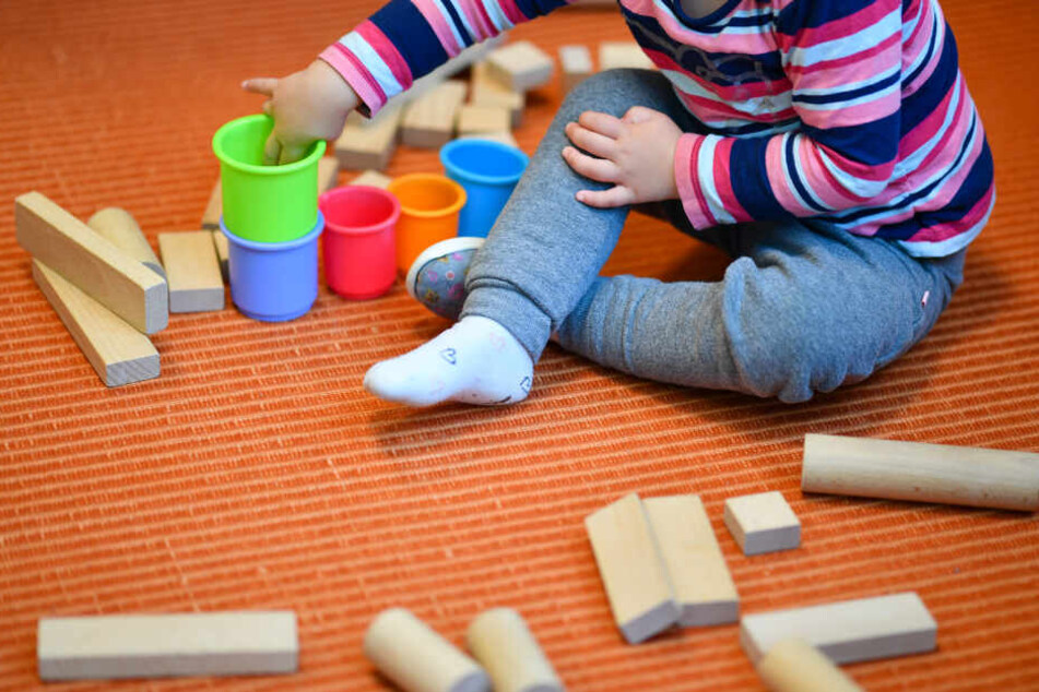 Ein Mädchen spielt in einer Kita mit bunten Bechern und Bauklötzen.