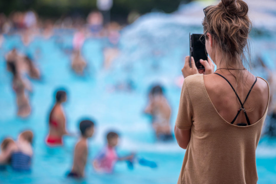 Eine junge Frau fotografiert mit ihrem Handy im Prinzenbad ihr schwimmenden Kinder.
