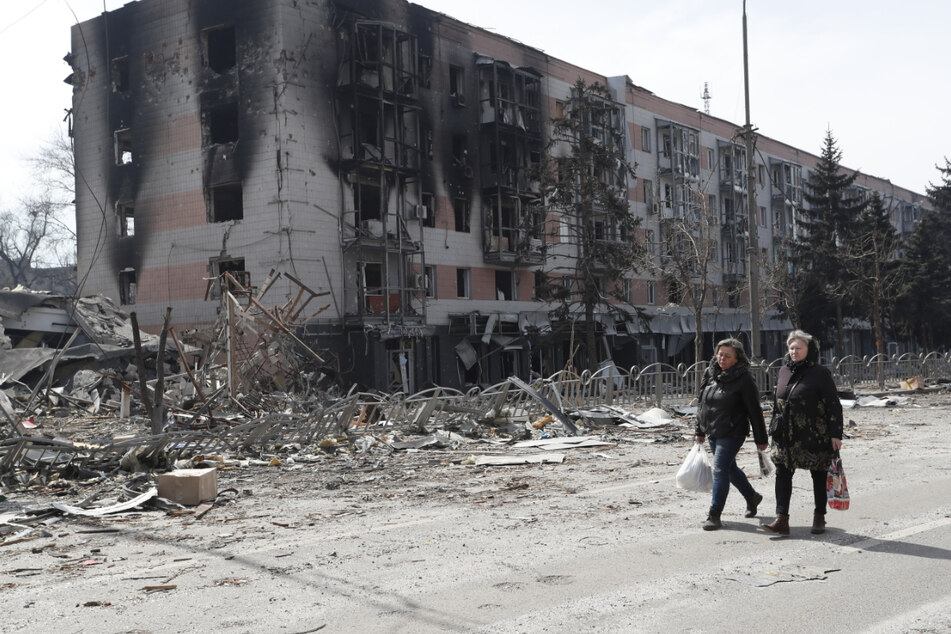Bewohner von Mariupol gehen an stark beschädigten Gebäuden entlang.