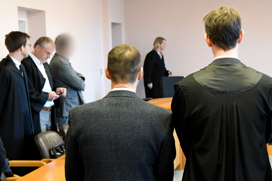 Zwei der Angeklagten (3.v.l und 4.v.l) stehen im Saal des Landgerichtes. In dem Prozess geht es um unrechtmäßige Pistolenlieferungen nach Kolumbien.