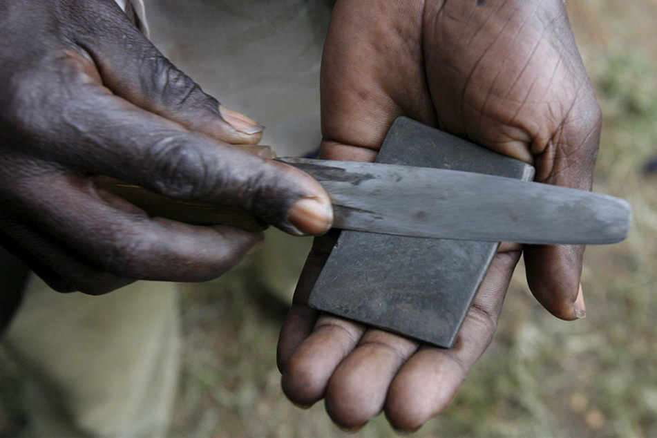 Ein Mann in Bungoma (Kenia) schärft sein Messer für die Beschneidung eines Jungen.