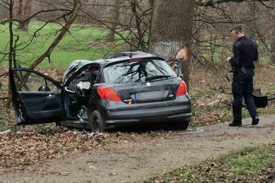 Ein Polizist steht neben dem Auto, das gegen einen Baum prallte.