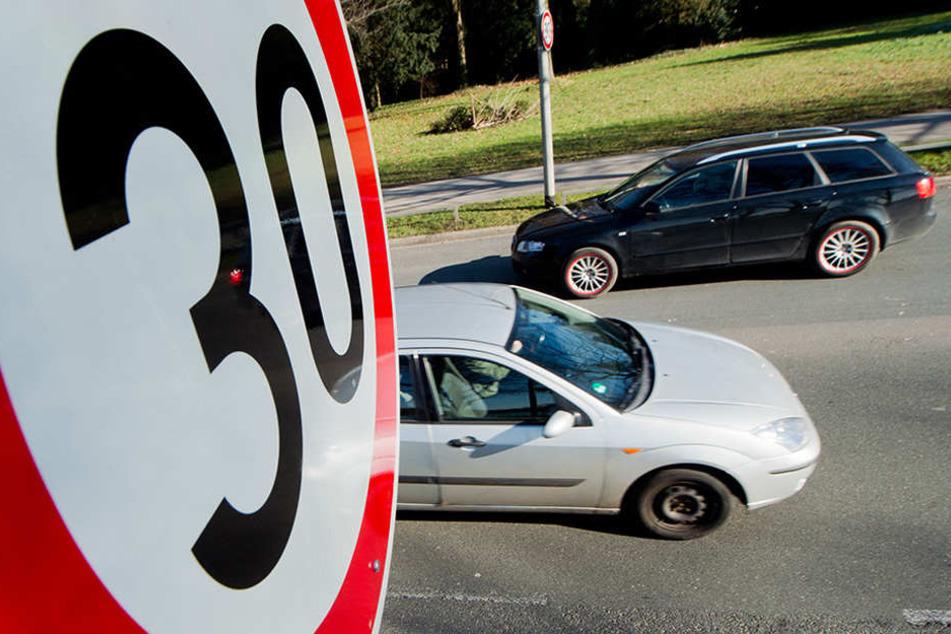 Autos fahren an einem Verkehrsschild für eine Geschwindigkeitsbegrenzung von 30 Stundenkilometer an Straße vor einer Schule vorbei.