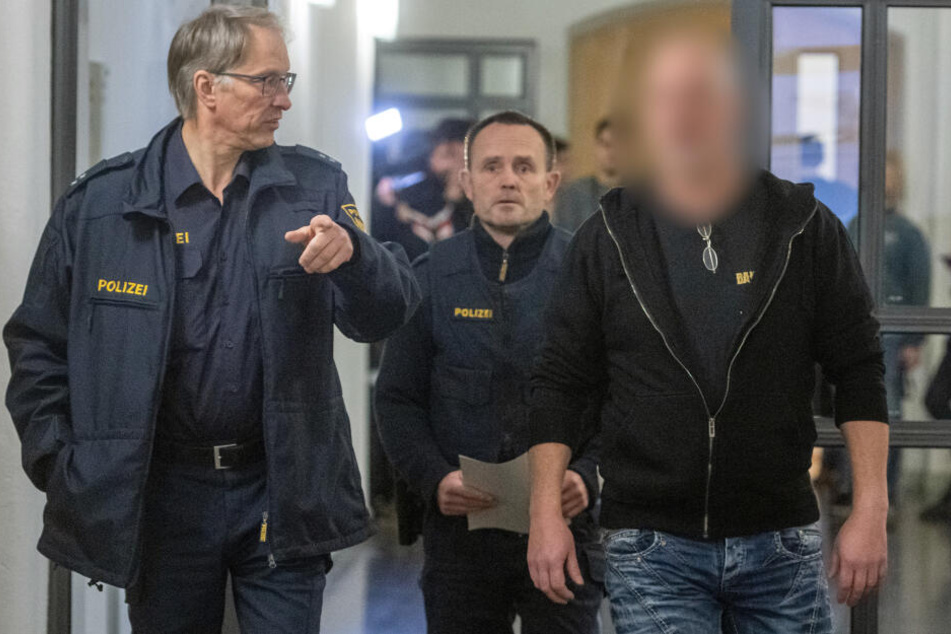 Der Angeklagte (r.) geht neben Polizisten in den Verhandlungssaal des Landgerichts.