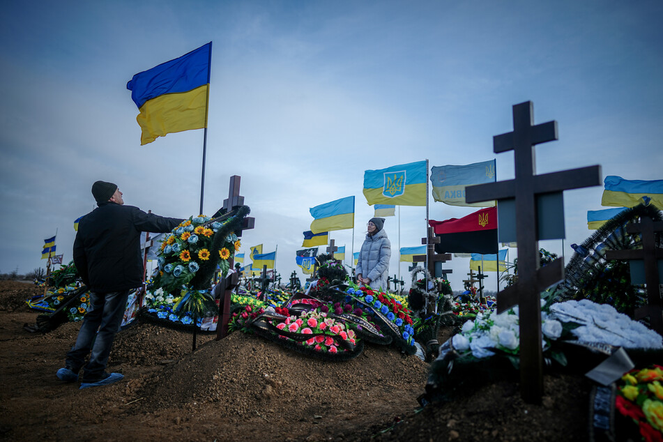 Anna, die Ehefrau eines vor zwei Monaten getöteten Soldaten, und der Vater Oleksandr stellen auf dem Friedhof der Hafenstadt Odessa die Ukrainische Nationalflagge am Grab ihres Ehemannes auf. (Archivbild)