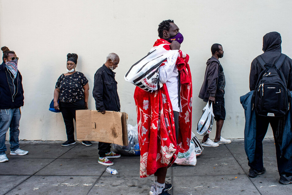People who live on the streets of Skid Row waiting in line with others to receive a boxed Thanksgiving meal, a bag of food, a blanket, and hygiene kits in November 2020.