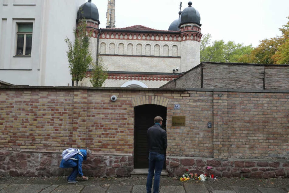 Menschen legen vor der Synagoge in Halle Blumen nieder.