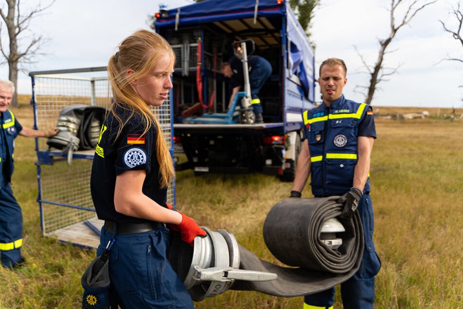 Eine ehrenamtliche THW-Helferin arbeitet im nordsächsischen Arzberg Hand in Hand mit ihren Kameraden beim Aufbau einer Wasserstrecke zur Brandbekämpfung.