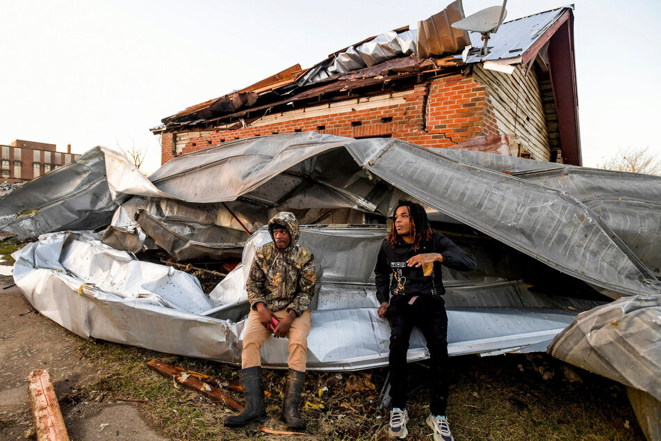 Cordel Tyus and Devo McGraw sit on roofing that blew off of an industrial building and wrapped around their house after a tornado ripped through Selma, Alabama, on January 12, 2023.