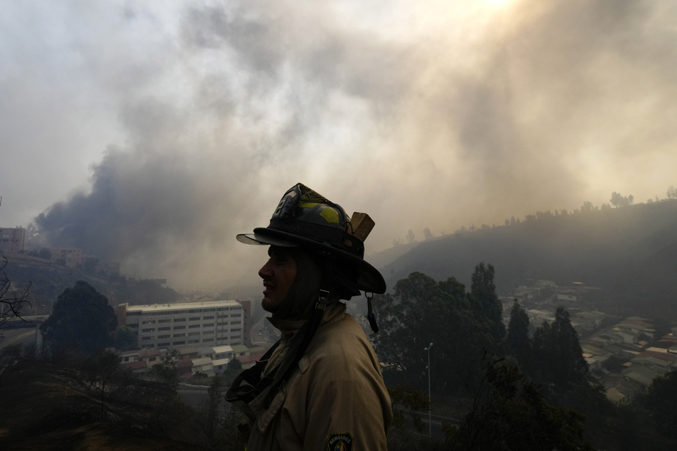 Ein Feuerwehrmann zeichnet sich gegen den rauchgefüllten Himmel ab, während sich ein Waldbrand ausbreitet.