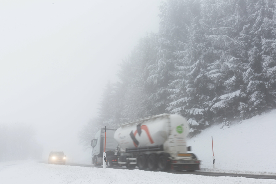 Ein LKW und ein Auto fahren im dichten Nebel auf der Landesstraße L128 im Schwarzwald durch die verschneite Landschaft.