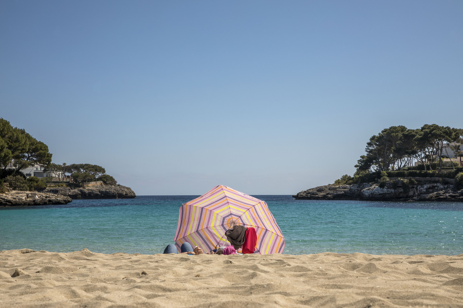 Zwei Personen liegen unter einem Sonnenschirm an einem Strand auf Mallorca. Die Zahl der Corona-Neuinfektionen auf Mallorca und den anderen Balearen-Inseln ist nach offiziellen Angaben relativ niedrig geblieben.