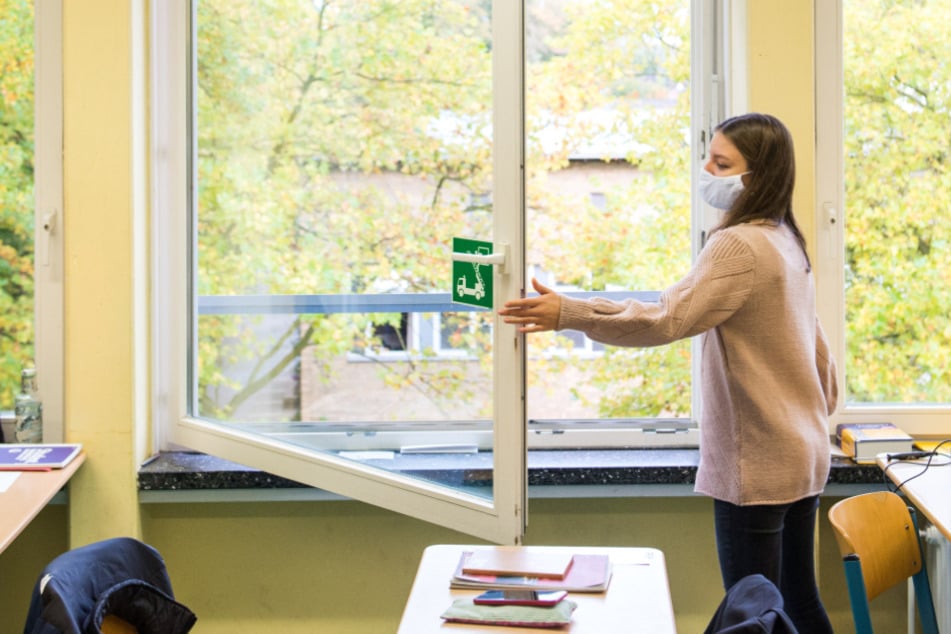 Eine Schülerin der Oberstufe öffnet mit einer Mund-Nasen-Bedeckung ein Fenster.