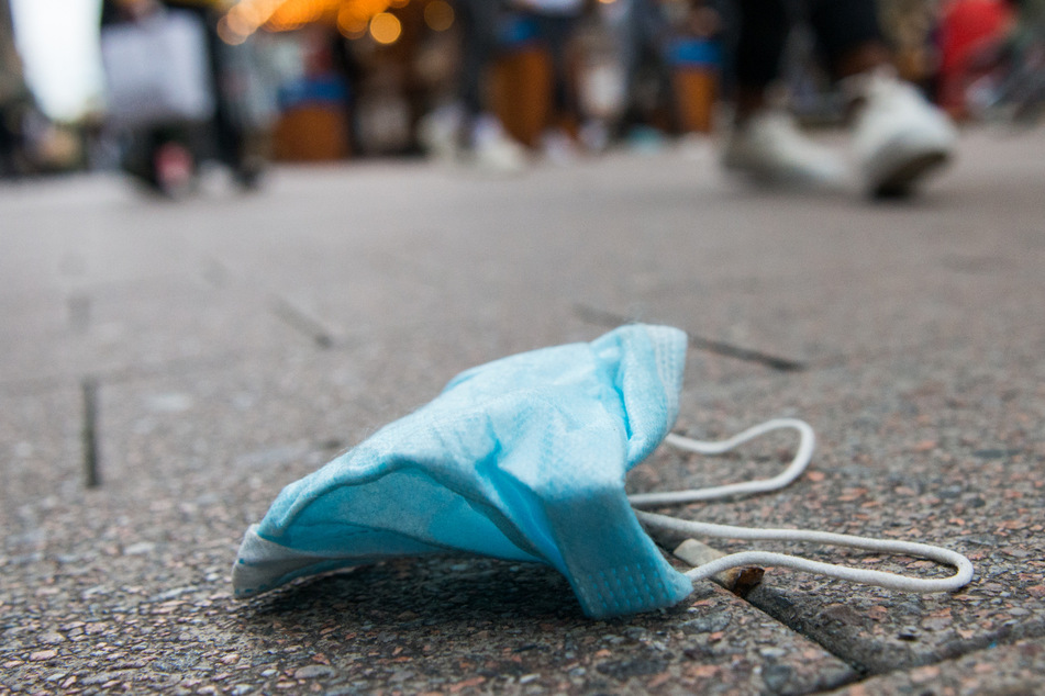 Eine medizinische Maske liegt auf dem Boden. In Thüringen hat die Zahl an Neuinfektionen mit der hochansteckenden Virus-Variante aus Indien zugenommen. (Symbolbild)