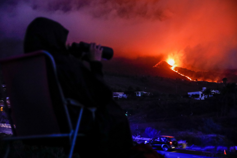 Eine Person sitzt auf einem Campingstuhl und beobachtet den Vulkan Cumbre Vieja, der Lava ausstößt.
