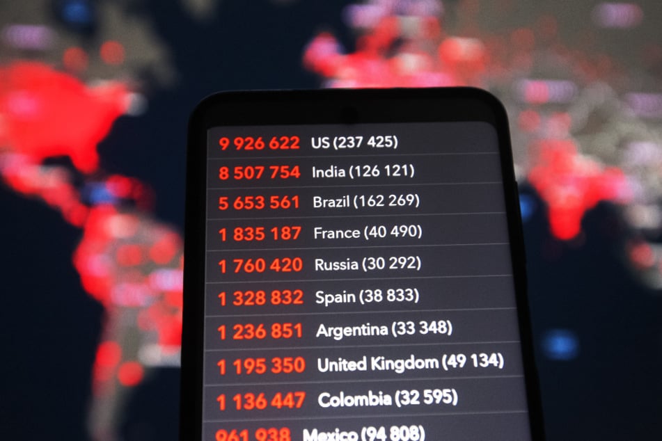 Auf einem Smartphone werden die Zahlen von Fälle von Corona-Infizierten und Corona-Toten verschiedener Länder von der Worldometer-Website gezeigt vor dem Hintergrund einer Karte des Center for Systems Science and Engineering (CSSE) an der Johns Hopkins Universität (JHU).