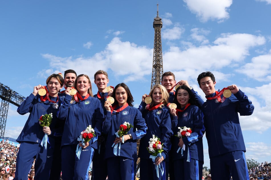 Members of the US figure skating team pose with their gold medals following the reallocation of medals from the Beijing 2022 Olympic Winter Games at the Paris 2024 Olympic Games in Paris on Wednesday, August 7, 2024 with the Eiffel Tower visible in the background.