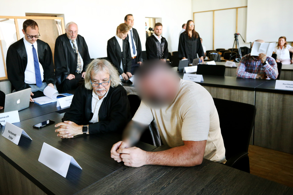 Zwei der sechs Angeklagten (vorne r. und hinten r.) warten auf den Beginn des Prozesses im Duisburger Landgericht.