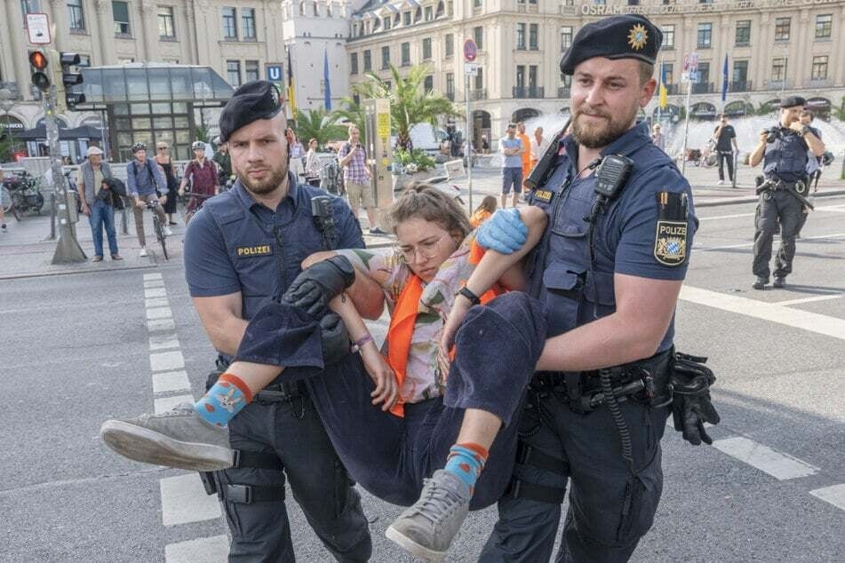 Klimaschutz gegen Bevölkerungsschutz: Eine Aktivistin wird von zwei Beamten auf dem Münchner Stachus von der Straße getragen.