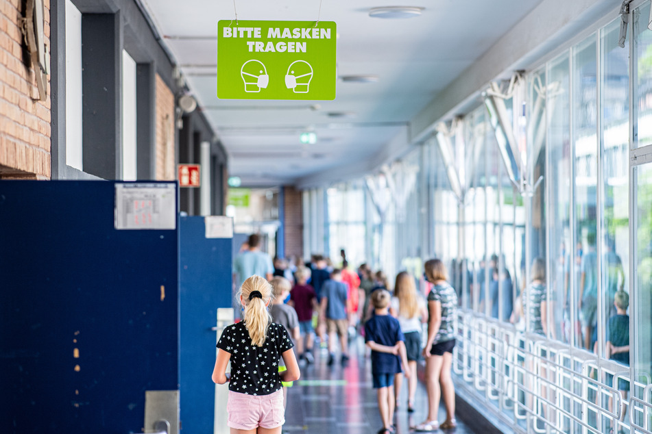 Auf dem Flur einer Schule hängt ein Schild mit der Aufschrift: "Bitte Masken tragen".