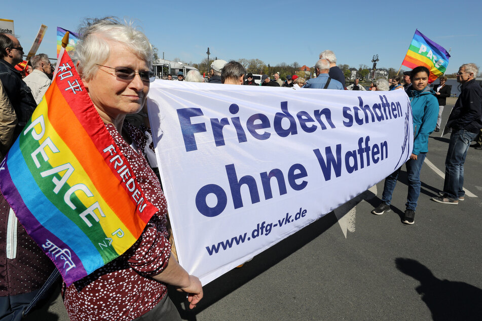 Menschen gehen mit Fahnen der internationalen Friedensbewegung in Rostock auf die Straße.