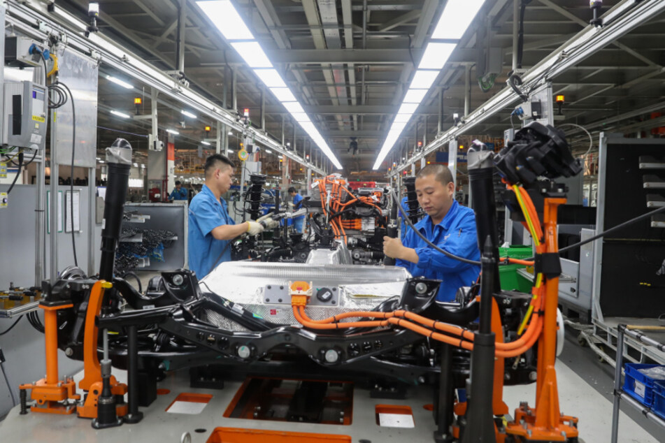 China, Shanghai: Fahrzeugbauer arbeiten in einer Werkshalle an einer Produktionslinie von SAIC Volkswagen.