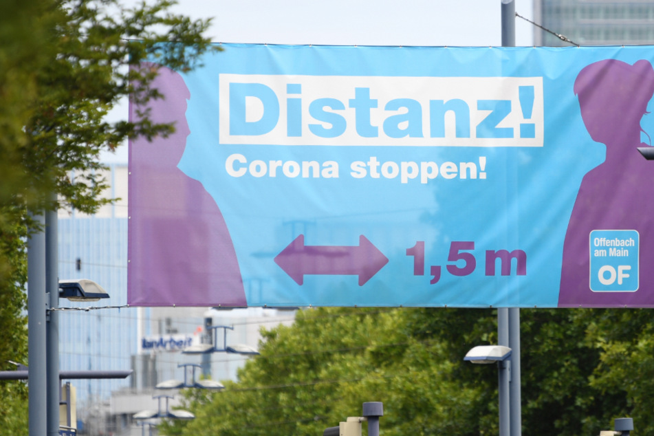 Ein großes Plakat mit der Aufschrift "Distanz! Corona stoppen !" prangt am Ortseingang von Offenbach über einer Straßenkreuzung.