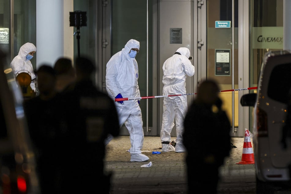 Mitarbeiter der Spurensicherung untersuchen den Tatort rund um das Kino, wo der Angreifer zuvor mit Brandsätzen um sich geworfen hatte.