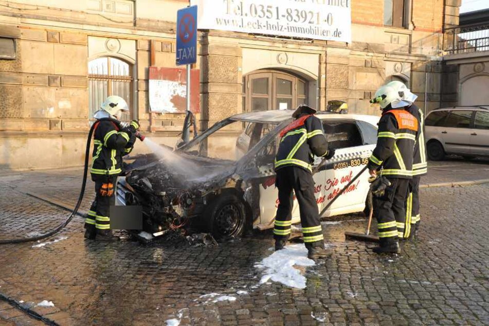Feuerwehrleute löschen das völlig zerstörte Taxi.