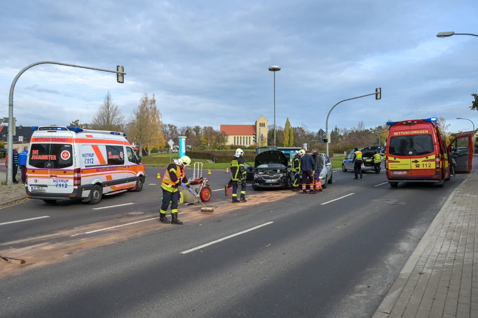 Die Feuerwehr säubert die Straße. Dahinter stehen die beiden Autos stehen nebeneinander.