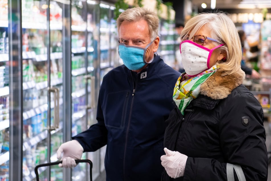 Ein Mann und eine Frau tragen bei ihrem Einkauf in einem Supermarkt einen Mundschutz.