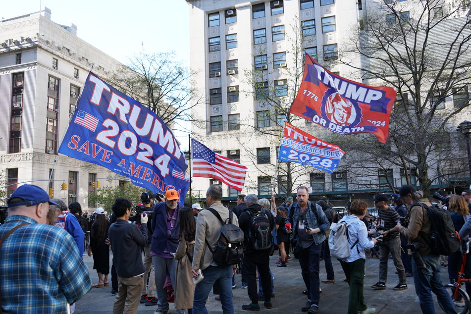 Donald Trump supporters holding large flags and speaking with media while protesting his hush money trial in New York City on April 15, 2024.