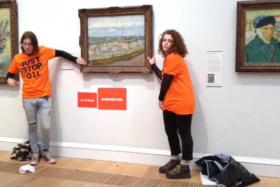 Emily Brocklebank (r.) and Louis McKechnie glue themselves to the frame of Van Gogh's Peach Trees In Blossom at London's Courtauld Gallery on June 30, 2022.