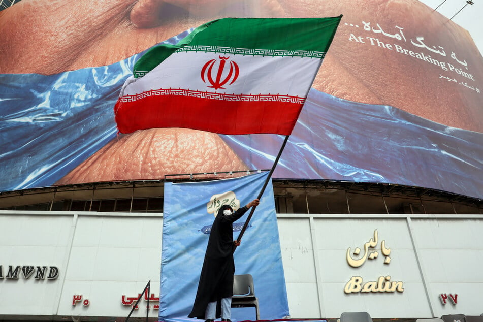 A woman waves an Iranian flag in front of an anti-US billboard referring to Donald Trump and the Strait of Hormuz in Tehran on Tuesday.
