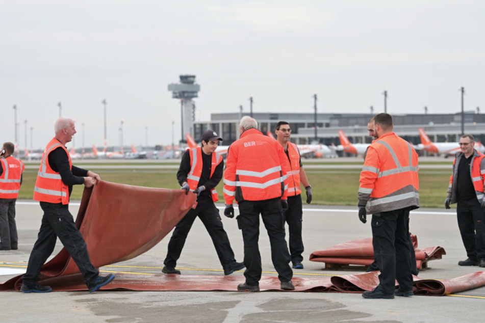 Arbeiter des Flughafens Berlin Brandenburg Willy Brandt (BER) legen auf der Startbahn Süd die Sperrkreuze zusammen und transportieren die Kunststoffplanen ab.