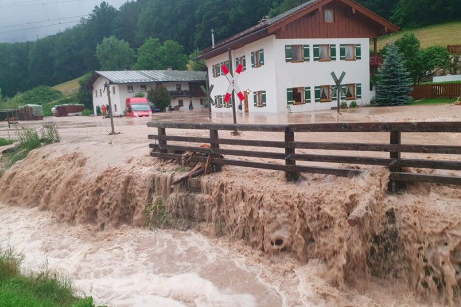 Wasser fließt über einen Platz vor einem Haus. Der Landkreis Berchtesgadener Land hat nach starkem Regen wegen Hochwassers den Katastrophenfall ausgerufen.