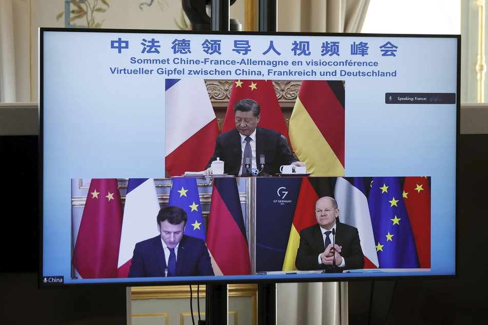 Ein Monitor zeigt Emmanuel Macron (44,unten,l), Präsident von Frankreich, Bundeskanzler Olaf Scholz (63, SPD, unten,r) und Xi Jinping (68,oben), Präsidenten von China, während einer Videokonferenz zur Ukraine-Krise.