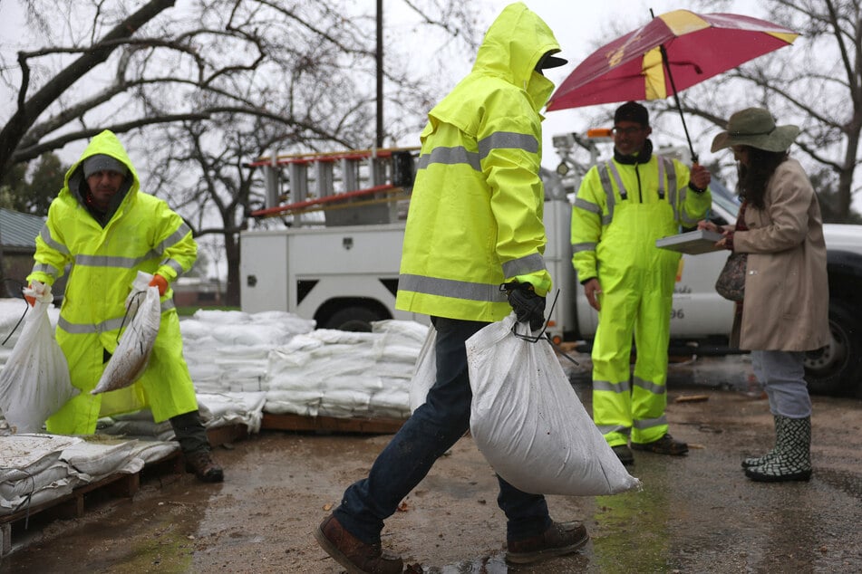 Los Angeles County workers load sandbags for a resident (R) near the Eaton Fire burn zone as a powerful atmospheric river storm impacts the region on Thursday in Pasadena, California.