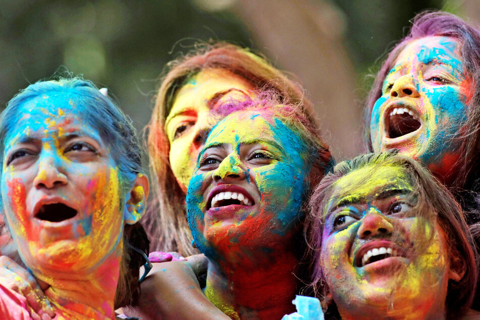 Frauen, deren Gesichter mit farbigem Puder beschmiert sind, jubeln während der Feierlichkeiten zum Holi-Fest in Mumbai, Indien.
