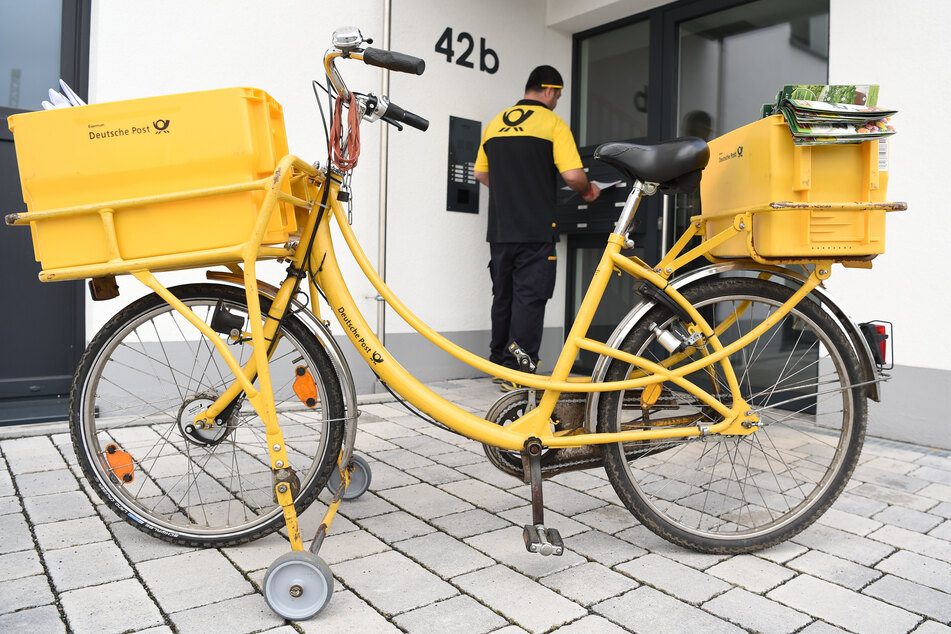 Ein Zusteller der Deutschen Post steht vor einem Wohnhaus.