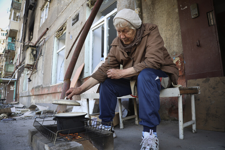 Eine Frau kocht im Hof ihres beschädigten Wohnhauses in Mariupol.